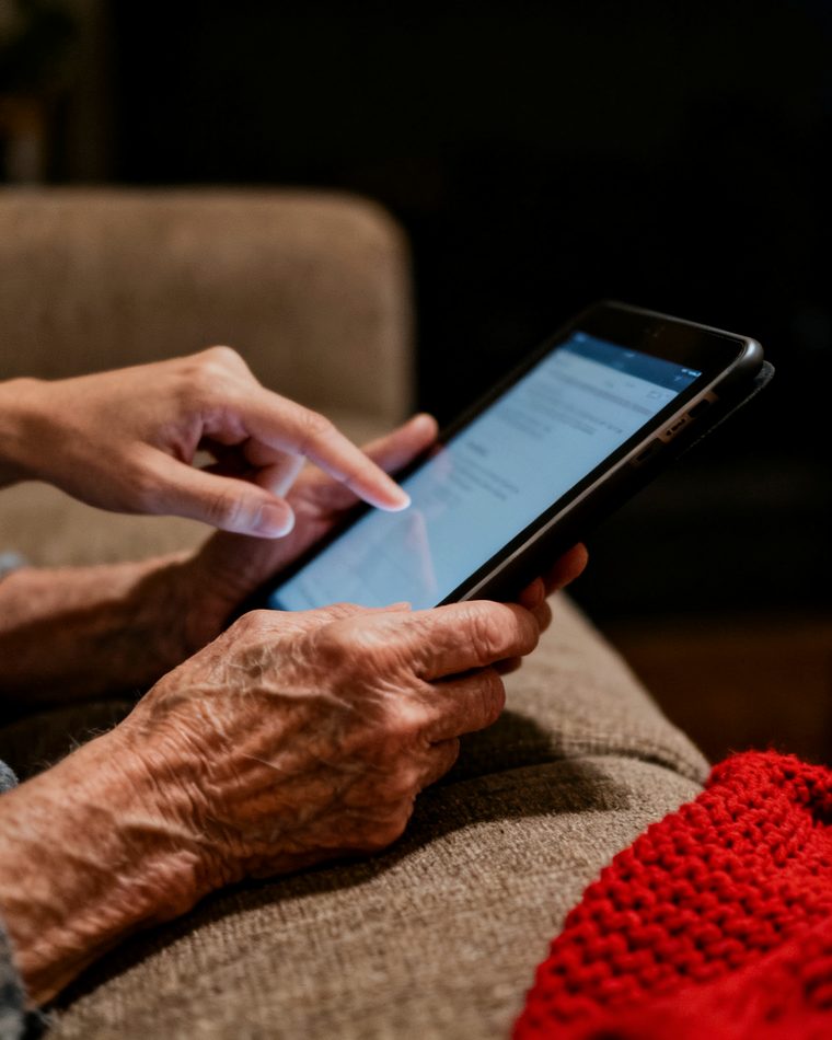 Ältere Hände mit Tablet, eine jüngere Hand zeigt auf den Bildschirm